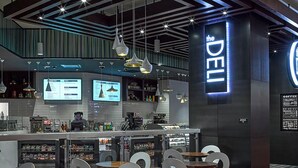 A modern bar area with a prominent 'DELI' sign, a digital menu display, and a seating area with chairs and tables. - Bally’s Evansville Casino & Hotel (Evansville)