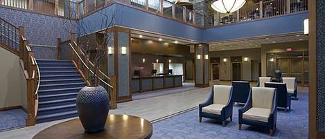 A spacious lobby with a central round table, a staircase, and multiple seating areas.