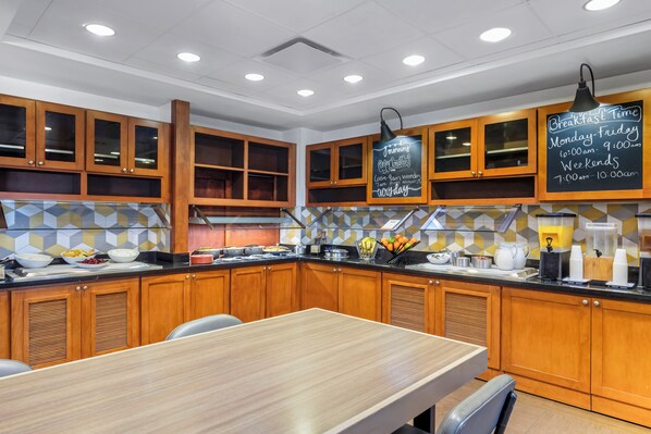 Una cocina moderna con armarios de madera, una barra desayunadora y una pizarra con los horarios del desayuno.