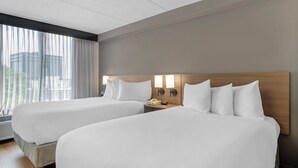 Une chambre d’hôtel avec deux lits, une table de chevet avec un téléphone et une fenêtre avec des rideaux.