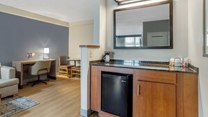 Une chambre d’hôtel compacte comprenant un coin cuisine, un bureau, une chaise, un petit réfrigérateur et un grand miroir.