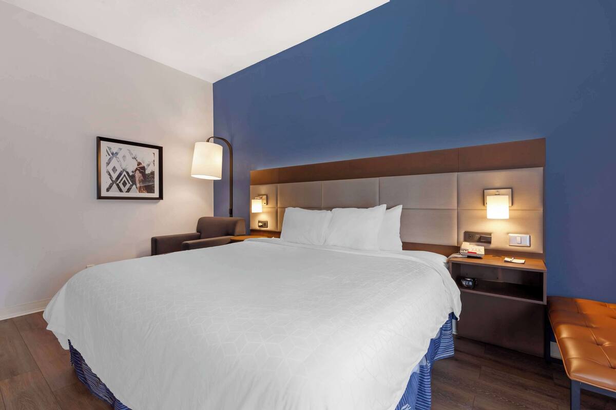 A hotel room with a large bed, two bedside tables, a bench, and a wall-mounted lamp.