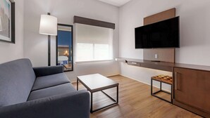 A modern living room with a sofa, a coffee table, a TV mounted on a cabinet, and a window with blinds.