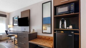A hotel room with a desk, a flat-screen TV, a sofa, a microwave, a coffee maker, and a refrigerator.