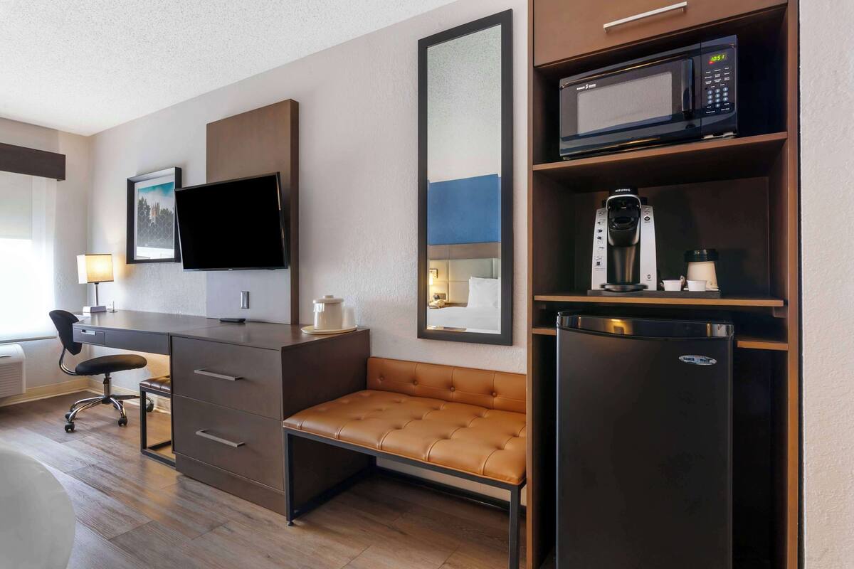A hotel room with a desk, a flat-screen TV, a sofa, a microwave, a coffee maker, and a refrigerator.