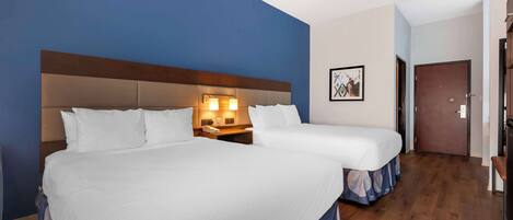 A hotel room with two beds, a wooden floor, and a blue accent wall.