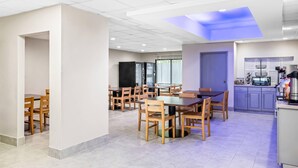 Un grand espace à manger avec de nombreuses tables et chaises en bois, un coin cuisine équipé d’appareils modernes et un plafond agrémenté d’une lucarne illuminée de lumière bleue.