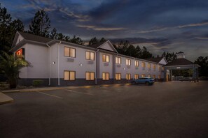 Un hôtel à plusieurs étages, avec une rangée de chambres, un parking couvert et un petit bâtiment surmonté d’une horloge.