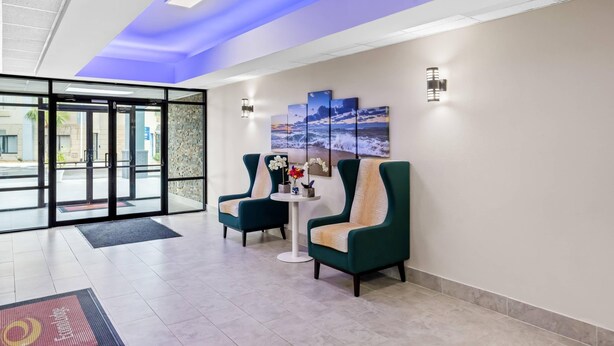 Un hall d’entrée avec une façade vitrée, des fauteuils turquoise, une petite table ronde ornée d’un vase de fleurs et une œuvre d’art accrochée au mur.
