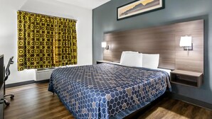 Une chambre d’hôtel avec un grand lit, une tête de lit dotée d’un éclairage intégré, une fenêtre avec des rideaux à motifs et un tableau accroché au mur.