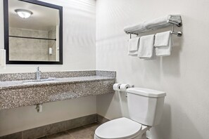 Un baño con lavamanos de encimera de granito, un inodoro, toallero con toallas y un espejo con marco negro.
