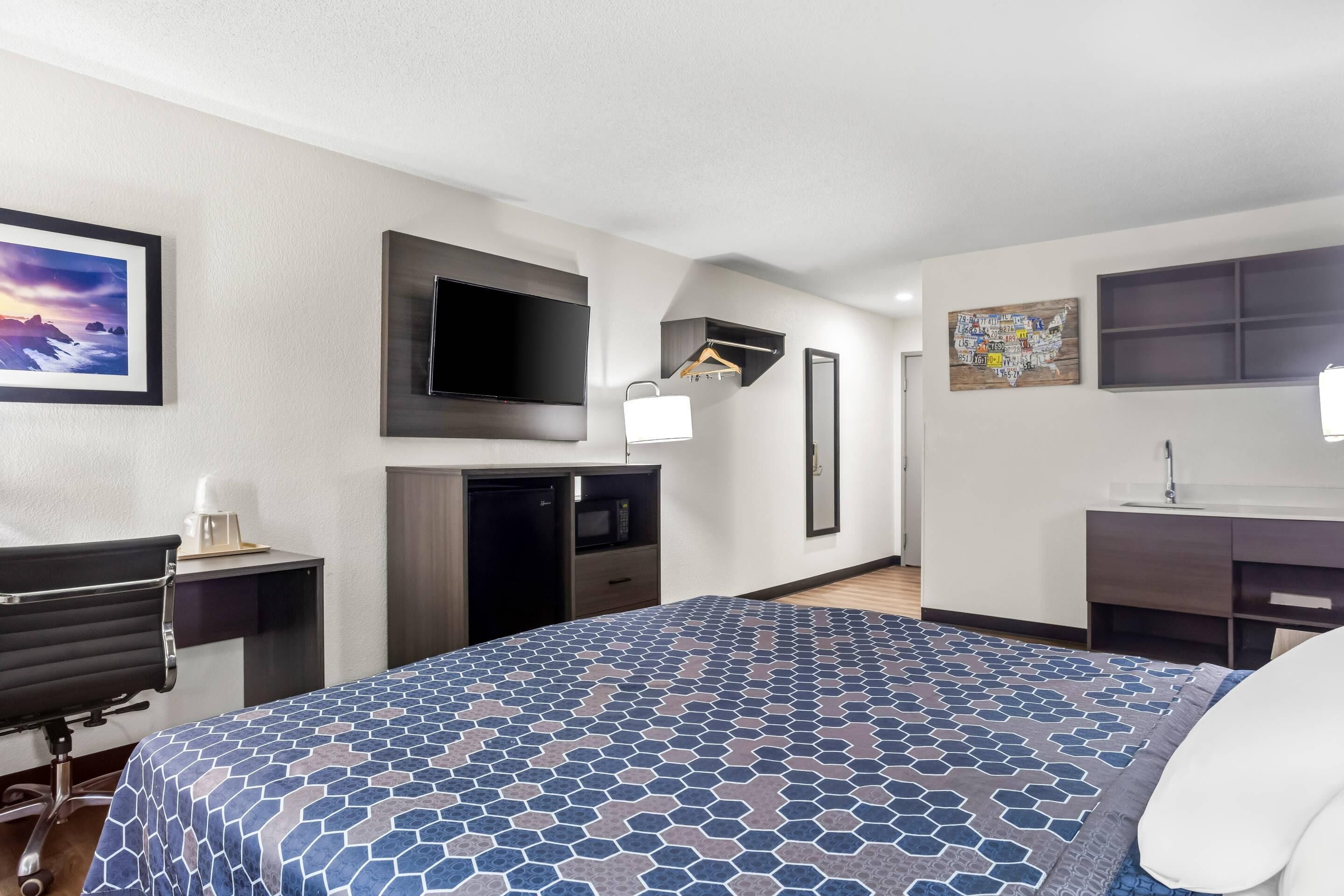 Una habitación de hotel con una cama, un escritorio con una silla, un televisor, un armario, un espejo y un estante pequeño con un mapa.