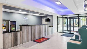 Un espace d’accueil comprenant un comptoir de réception en bois, un écran numérique et une porte vitrée donnant sur l’extérieur.