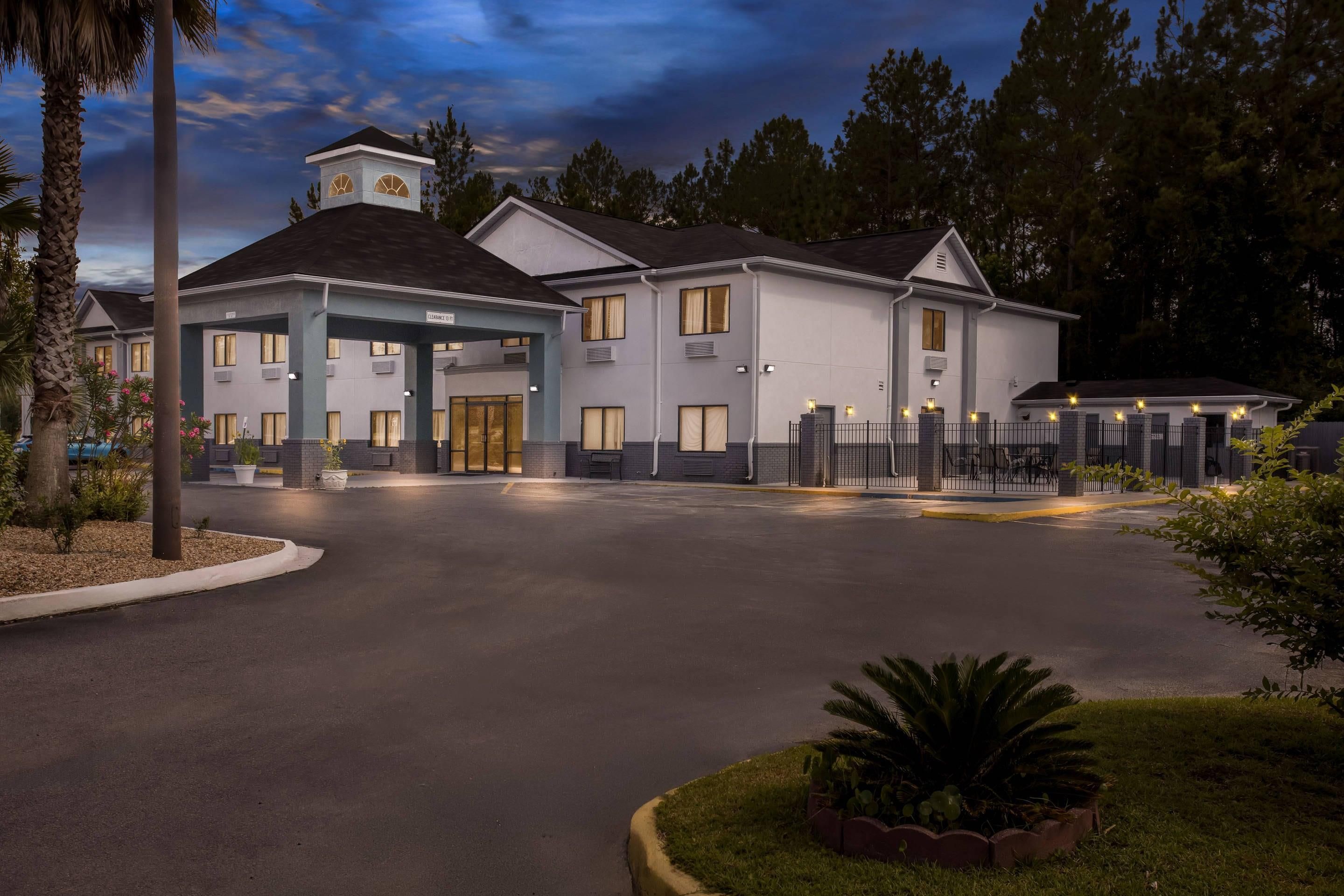 A hotel with a central building, a covered entrance, and a fenced parking area.