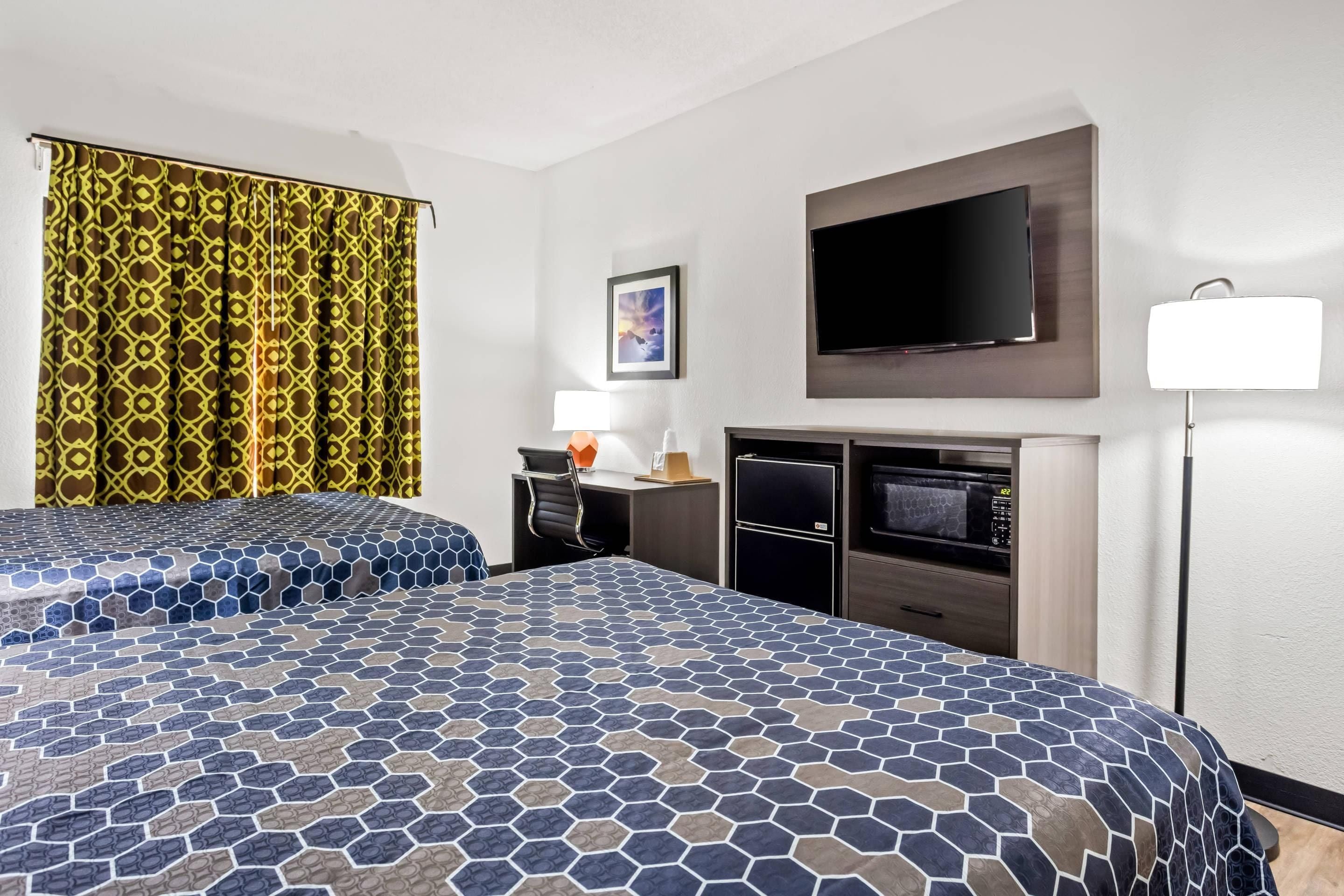 A hotel room with two beds, a flat-screen TV, a desk with a lamp, and a minibar.