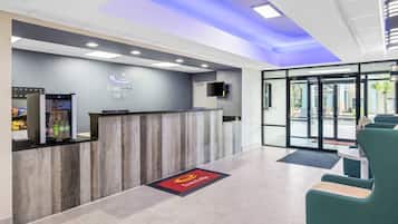 A reception area with a wooden reception desk, a digital screen, and a glass door leading outside.