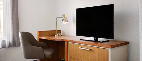 Et hotelværelse med skrivebord i træ, en moderne stol, et fladskærms-tv og en skrivebordslampe.