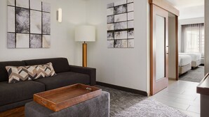 Une chambre d’hôtel moderne avec un canapé gris, une table d’appoint en bois et des œuvres d’art abstraites accrochées au mur.