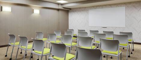 A conference room with rows of white chairs with yellow cushions, a whiteboard, and a carpeted floor.