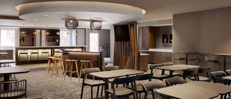 A modern restaurant with round tables, bar seating, and a central bar area.
