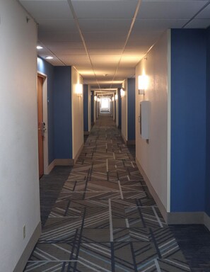 A hotel hallway with patterned carpet, blue walls, and doors on both sides. - Holiday Inn Express Henderson N Evansville South by IHG (Henderson)