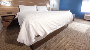 Een hotelkamer met een groot bed, een nachtkastje, een wandlamp en een raam met jaloezieën.