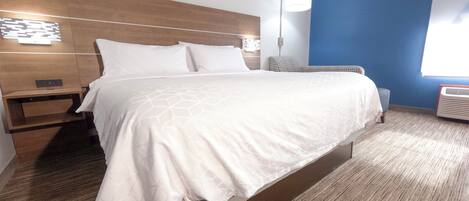 Una habitación de hotel con una cama grande, una mesita de noche, una lámpara de pared y un ventanal con persianas.