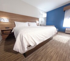 Una habitación de hotel con una cama grande, una mesita de noche, una lámpara de pared y un ventanal con persianas.
