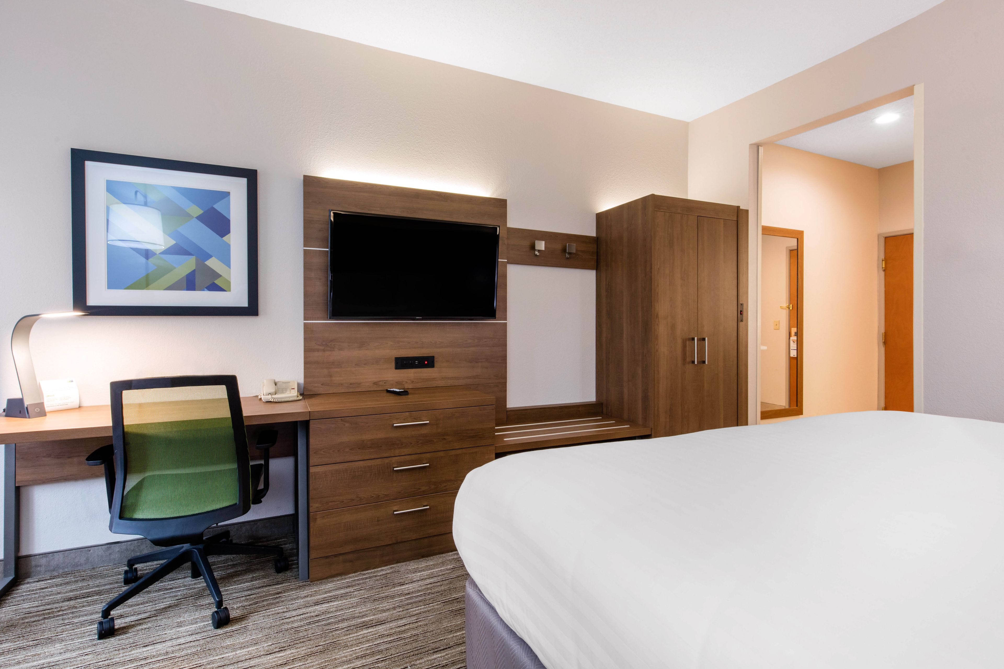 A hotel room with a bed, a desk with a chair, a television, and a wardrobe.