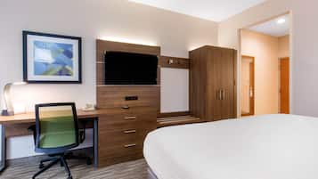 A hotel room with a bed, a desk with a chair, a television, and a wardrobe.