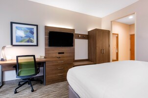 Una habitación de hotel con una cama, un escritorio con silla, televisor y armario.