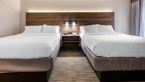 Une chambre d’hôtel avec deux lits, une tête de lit en bois, une table de chevet avec un téléphone et une fenêtre avec des rideaux.