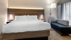 Une chambre d’hôtel avec un grand lit, une table de chevet avec une lampe, un canapé et une fenêtre avec des rideaux.