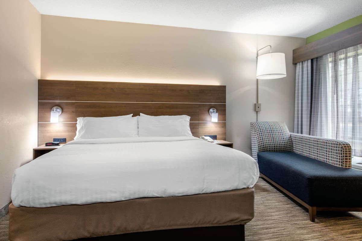 Una habitación de hotel con una cama grande, una mesita de noche con lámpara, un sofá y una ventana con cortinas.