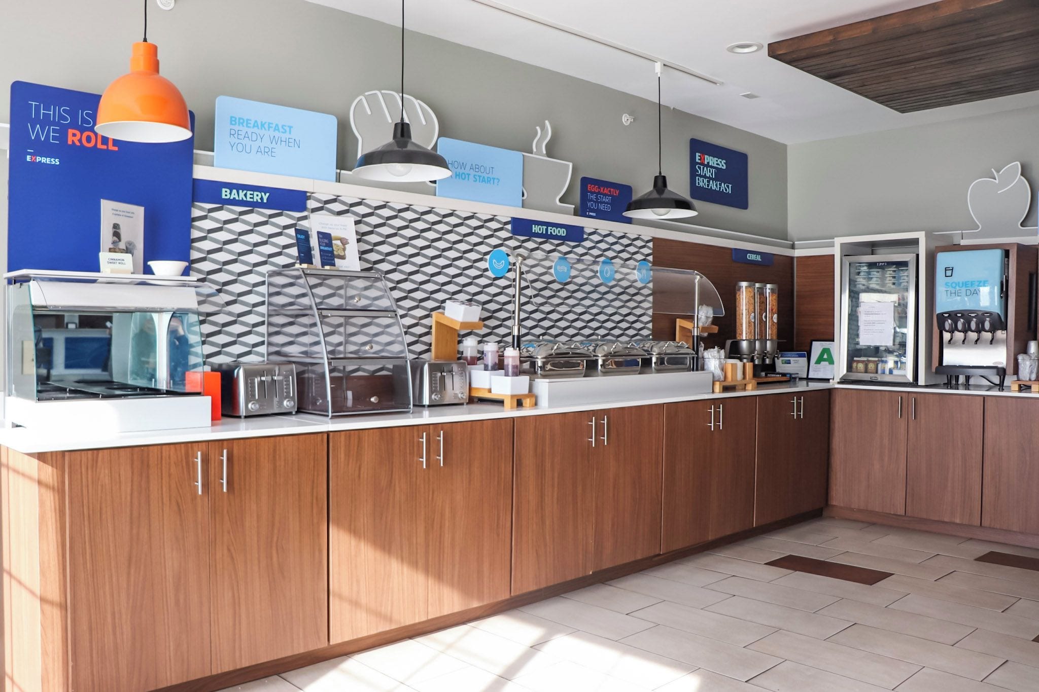 A modern breakfast area with a bakery counter, hot food station, and a beverage dispenser.