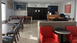 Un café moderne doté de plusieurs espaces de détente, notamment des tables et des chaises, un comptoir avec une machine à café et un téléviseur fixé au mur.