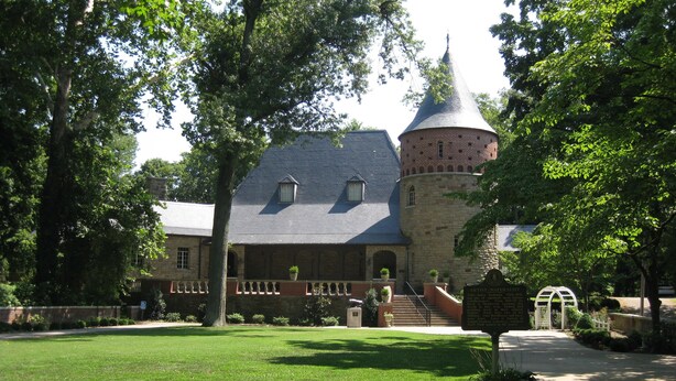Un bâtiment historique doté d’une tourelle et d’une façade en pierre, entouré d’une pelouse bien entretenue et d’arbres.