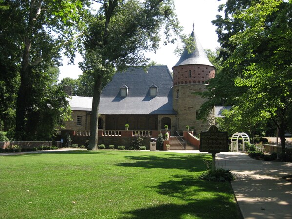 A historic building with a turret and a stone facade, surrounded by a well-maintained lawn and trees.