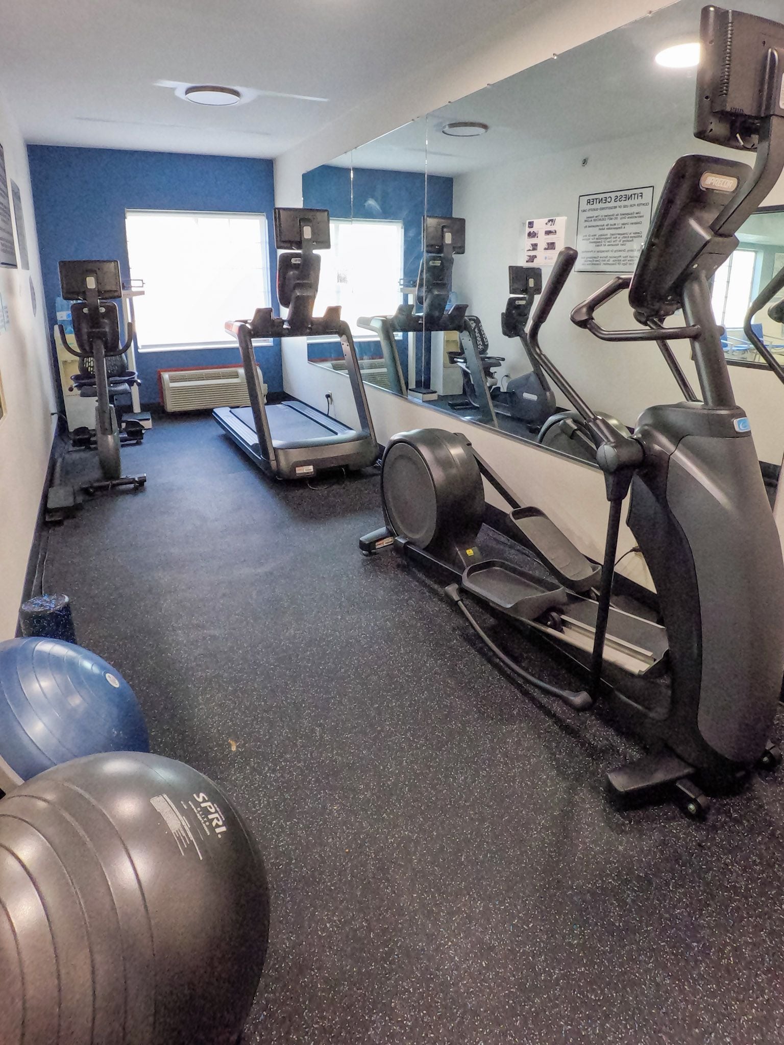 Un gimnasio con cintas de correr, elípticas y pelotas de ejercicio.