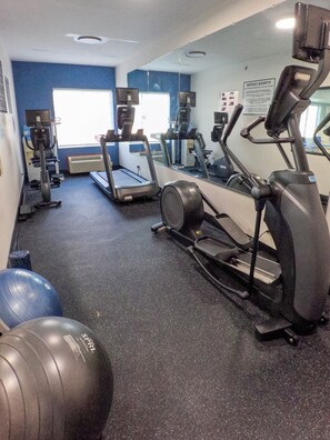 Une salle de sport équipée de tapis de course, de vélos elliptiques et de ballons d’exercice.