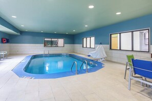 Una piscina interior con carriles delimitados, un vestuario con espejo y una zona de estar con sillas.