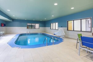 Una piscina interior con carriles delimitados, un vestuario con espejo y una zona de estar con sillas.