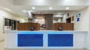 Un comptoir d’accueil d’hôtel avec deux guichets, un kiosque d’enregistrement numérique et une horloge murale.