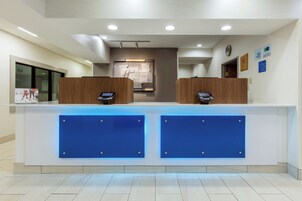 Un mostrador de recepción de hotel con dos mostradores, un quiosco de auto check-in y un reloj de pared.