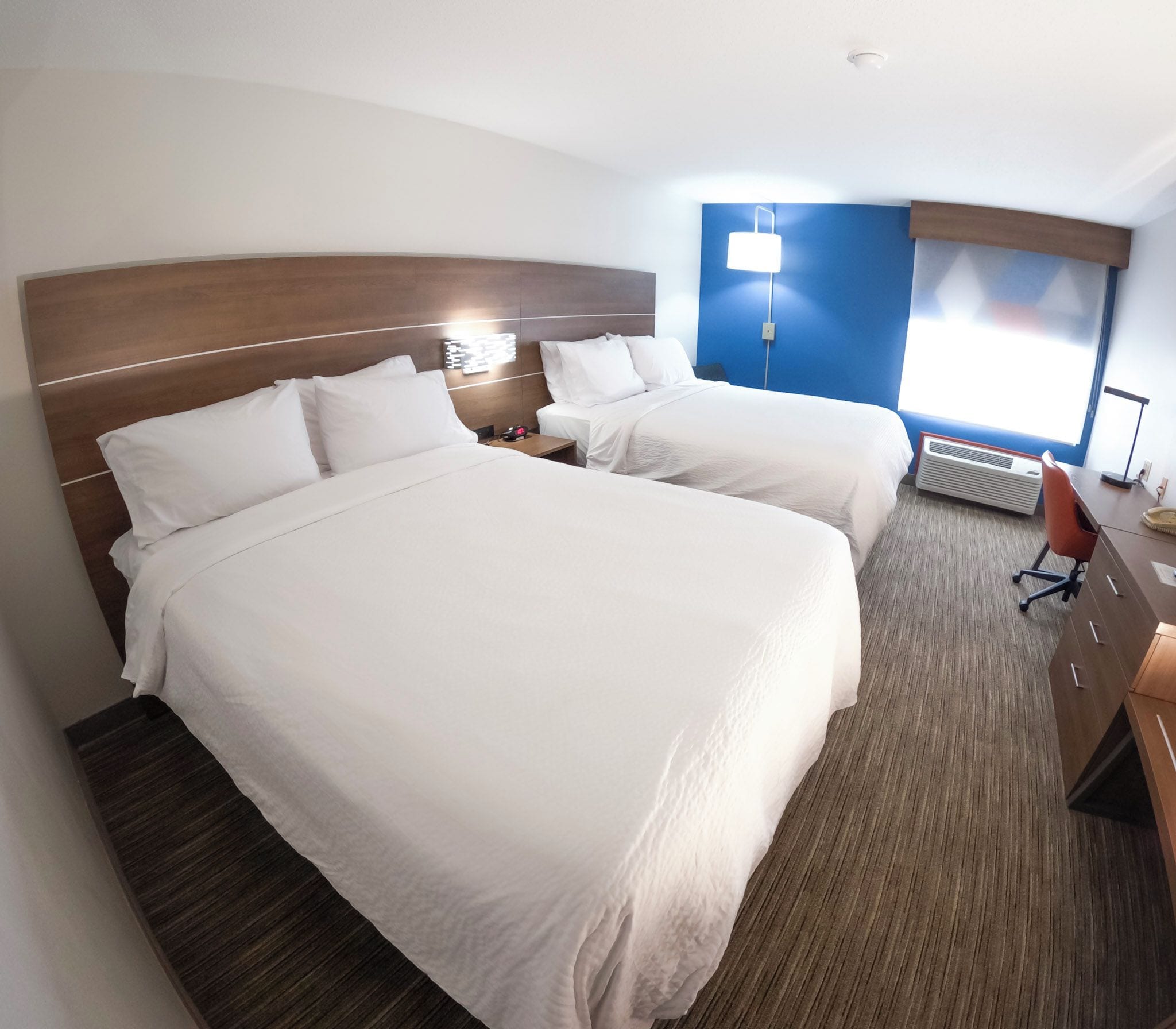 Ein Hotelzimmer mit zwei Betten, einem Schreibtisch, einem Stuhl und einem Fenster.