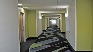 Un long couloir étroit, doté d’un tapis à motifs, avec des portes de part et d’autre et un éclairage fluorescent.
