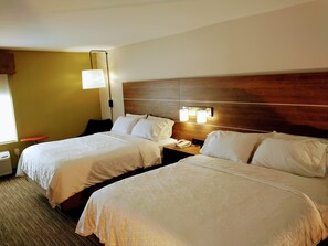 Habitación de hotel con dos camas, una mesita de noche con lámpara y una ventana con persianas.