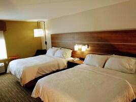 Habitación de hotel con dos camas, una mesita de noche con lámpara y una ventana con persianas.