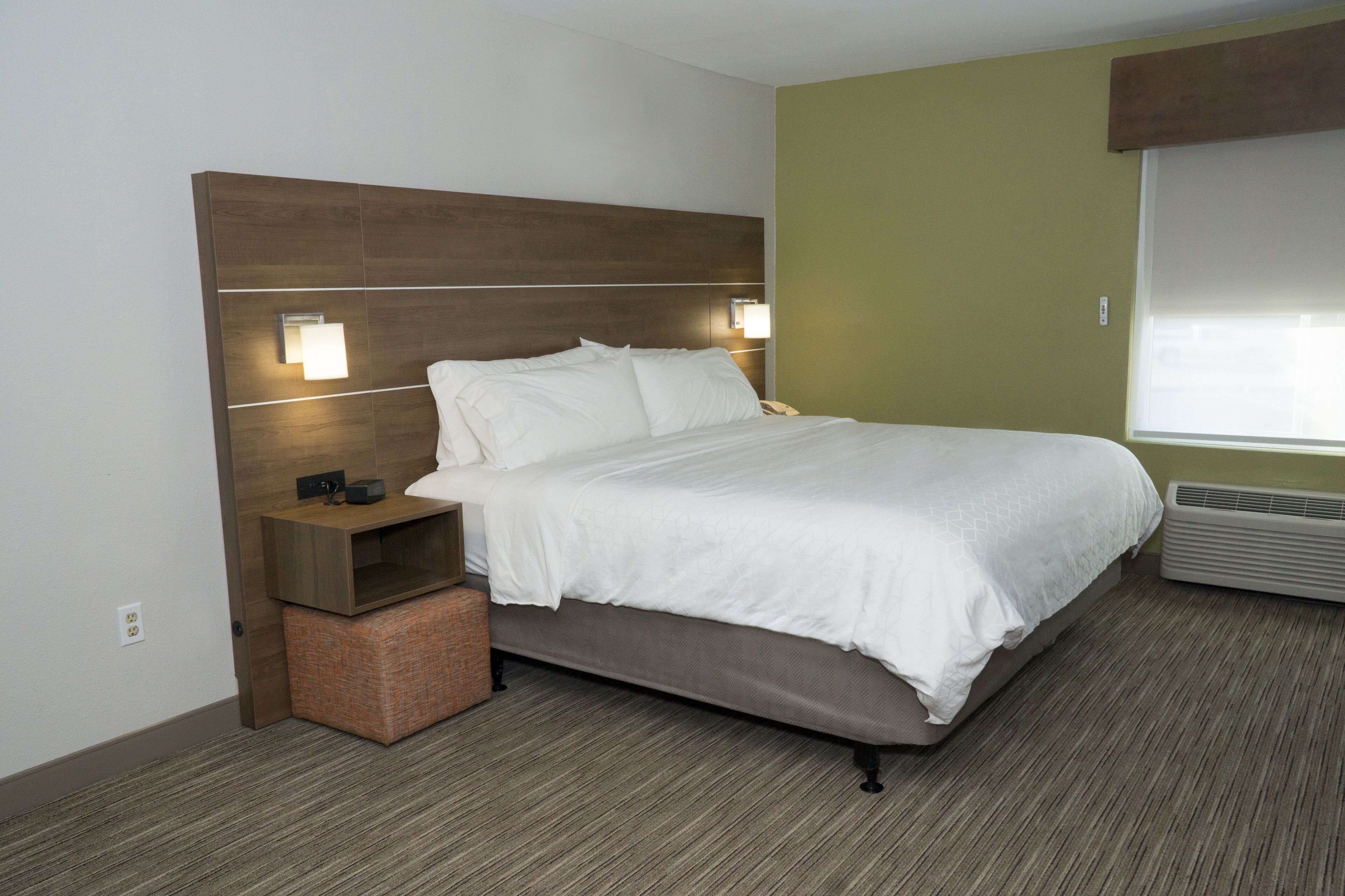 Una habitación de hotel con cama, mesitas de noche, una lámpara de pared y una ventana.
