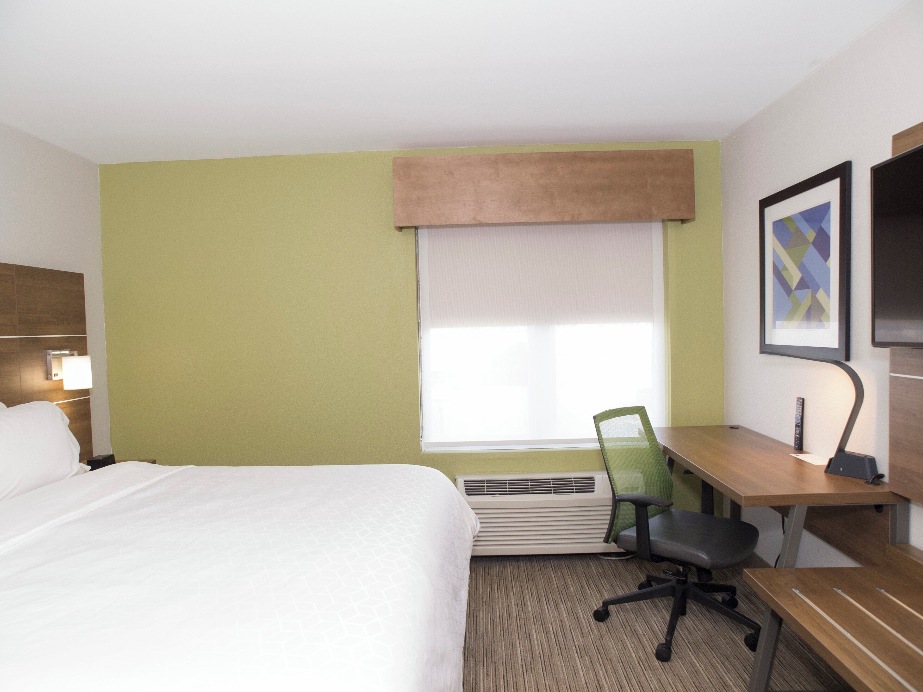 A hotel room with a bed, desk, chair, and a large window.